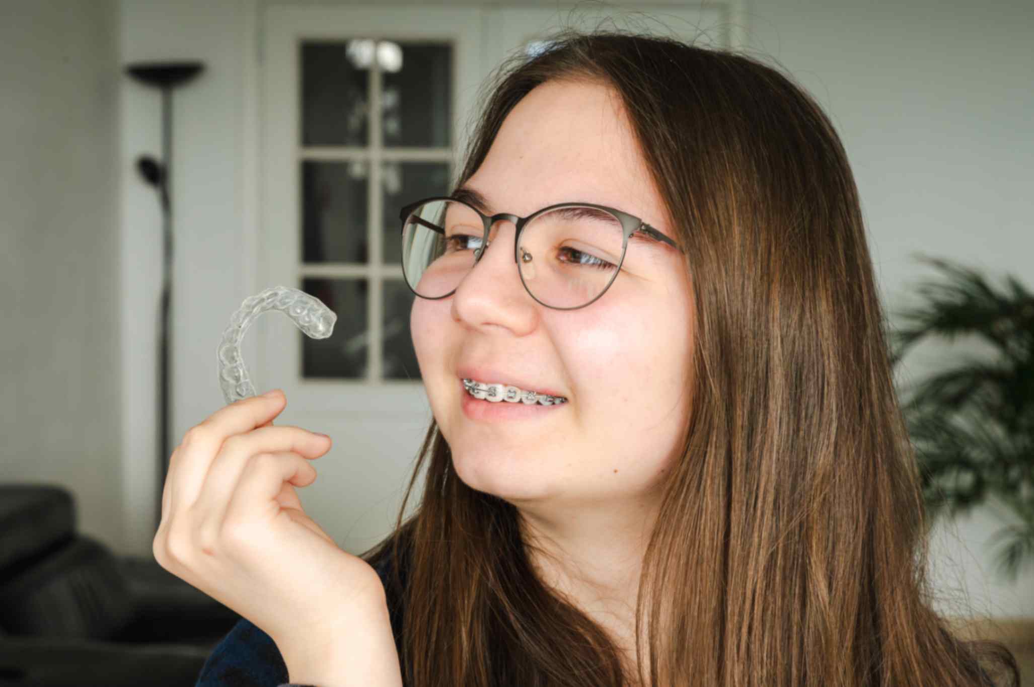 teenage-girl-holding-clear-aligner-and-showing-braces